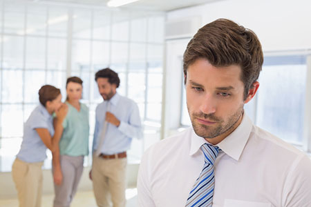 sad man with coworkers gossiping behind him