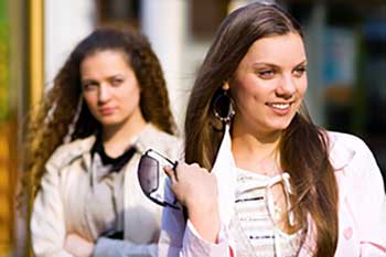 Girl standing behind another girl glaring at her.