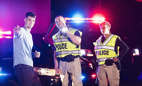 a male police officer and a female police officer talking to a young man at night with a police car with lights flashing behind them