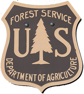 a brown US Department of Agriculture Forest Service badge with a tree in the center