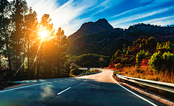 A sunset view from a road winding through a forest