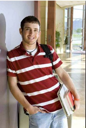 male student standing up against wall with books and backpack