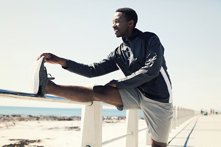 Man standing with leg up on hand rail, stretching.