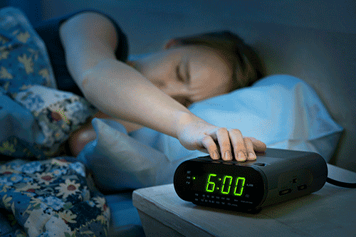 person reaching to shut alarm clock off