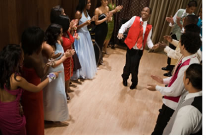 "Image of a teenage boy dancing while others cheer."